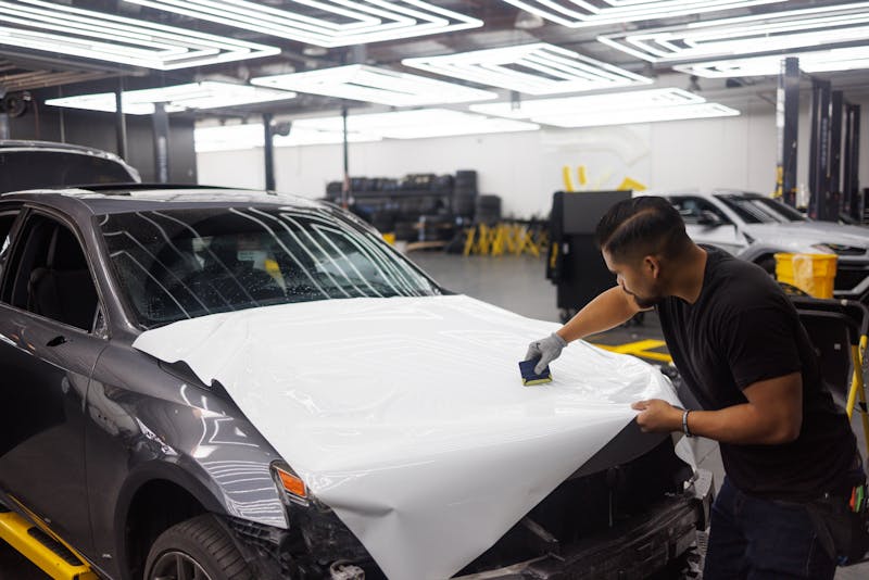 Professional technician applying vinyl wrap to car hood with proper technique